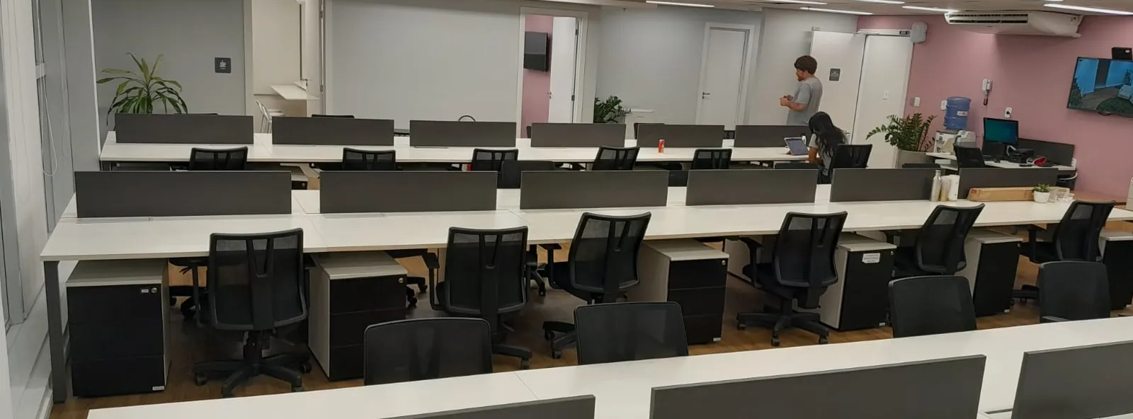 Pavimento corporativo concluído e em uso, com estações de trabalho, divisórias baixas e iluminação linear.