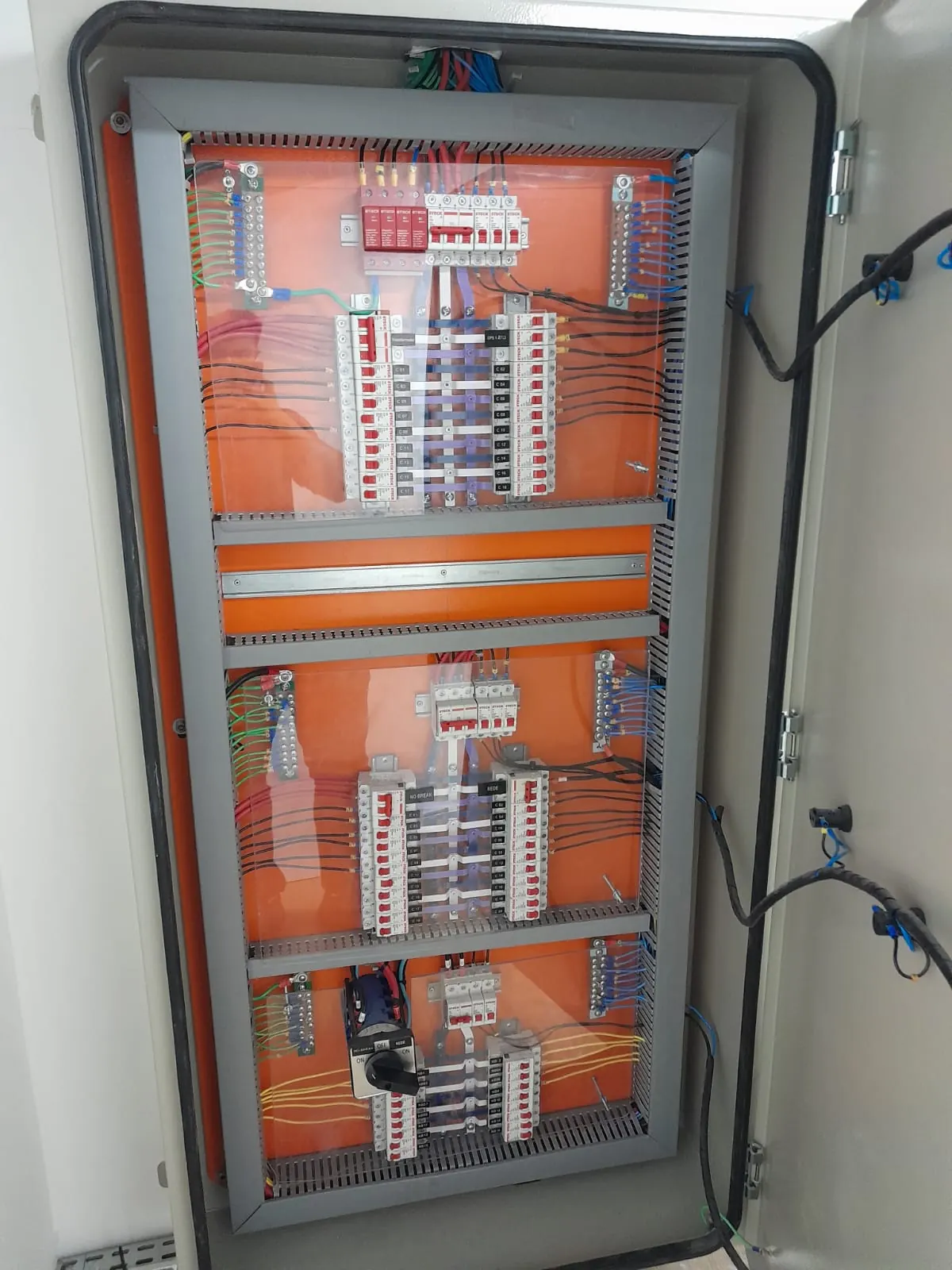 Quadro de distribuição elétrica aberto, com disjuntores e cabeamento identificados.